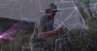 Kurak çalılıklarda çömelmiş bir adam, bitki örneklerini inceliyor, teknoloji ağı örtüsü gösteriyor. Doğa, keşif, yenilik, bağlantı, açık hava, araştırma, modern