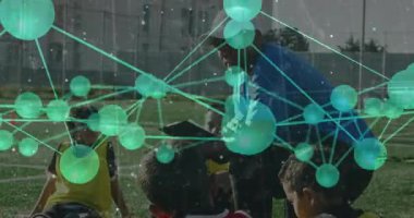 Koç, sahada diz çöküp, turuncu koni ve yeşil spor eğitimi alan çocukları eğitiyor. Koçluk, gençlik, takım çalışması, akıl hocalığı, açık hava, etkinlik, canlı