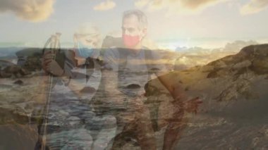 Kayalık kıyı günbatımında yüzen sağlık simgeleri ve verilerle kalp atış hızı grafiğini izleyen yürüyüşçüler. Açık hava, macera, refah, doğa, boş zaman, manzara, aktif