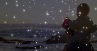 Anne, gün batımında kırmızı kovayla ve sağlık için yıldız ışıklarıyla omzunda bebek taşıyordu. Aile, şefkat, açık hava, sükunet, sıcaklık, manzara, bağ.