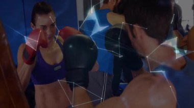 Kadın boksör fitness antrenmanında odak yastıklarına yumruk atıyor, dijital dünya ile örtüşüyor. Sporcular, güç, kararlılık, modern, yenilik, fitness, rekabet
