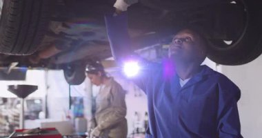 Araba tamirhanesinde araba şasisi teftiş eden kadın tamirciler yüzen çizelge simgeleriyle birlikte. Otomotiv, onarım, işyeri, sanayi, takım çalışması, teknoloji, profesyonel