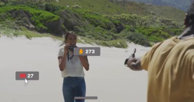 Kumsalda DSLR kamera taşıyan bir kadın, yüzen sosyal medya pazarlama uyarılarıyla çevrili. Fotoğraf, plaj, açık hava, yaşam tarzı, sosyal medya, teknoloji, macera