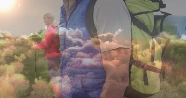 Çimenli yamaçta sarı sırt çantasıyla yürüyüş yapan olgun bir adam, yüzen sağlık verilerini gösteriyor. Macera, keşif, vahşi doğa, doğa, yürüyüş, dayanıklılık.