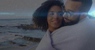 Günbatımında kayalık sahilde battaniyenin altında, sağlık için sarılan bir çift. Canlandırılmış kalp simgeleri havada süzülüyor. Romantizm, şefkat, samimiyet, sahil şeridi, alaca karanlık, doğal, huzur