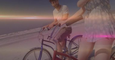 Gün batımında plajda bisiklete binen erkek ve kadın, yüzen kalp ikonu artı grafiğinin yer aldığı sağlığı resmediyor. Romantik, boş zaman, dinginlik, açık hava, canlı, aktif, yaşam tarzı