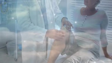 Erkek doktor, tıbbi klinikteki yaşlı kadın hasta dizini yüzen anatomi grafikleriyle inceliyor. Tıbbi, sağlık, ortopedi, klinik, muayene, terapi, sağlık