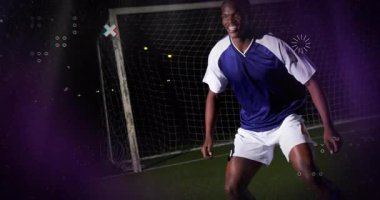 Erkek futbol kalecisi, spor teknolojisi veri örtüsünü gösteren ışıkların altında sahada öne eğiliyor. Atletik, rekabet, spor, kararlılık, gece hayatı, enerji, performans