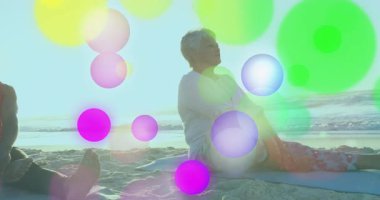 Sahilde bacak bacak üstüne atmış bir şekilde oturan yaşlı bir kadın mercek fişeğiyle sağlık yogası akışını gösteriyor. Sakinlik, rahatlama, refah, dinginlik, açık hava, farkındalık, ahenk.