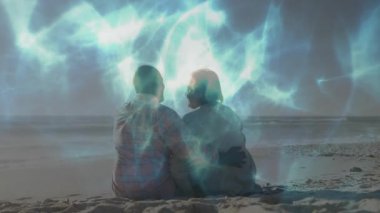 Sahilde oturup okyanusa bakan çift, animasyon mavi ışık desenleri ile teknoloji temasını gösteriyor. Romantizm, dinginlik, uyum, sükunet, bağlantı, sembolizm, doğal
