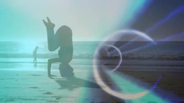 Güneşin doğuşunda kumlu sahilde amuda kalkan bir kadın. Animasyon ışık halkası sağlıklı olduğunu gösteriyor. Siluet, gündoğumu, plaj, okyanus, ışık efekti, doğal manzara, rahatlama