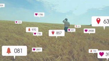 Buğday tarlasında duran adam, yüzen bildirim simgeleriyle pazarlama ölçümlerini analiz ediyor. Doğa, kırsal, manzara, iletişim, analitik, üretkenlik, teknoloji