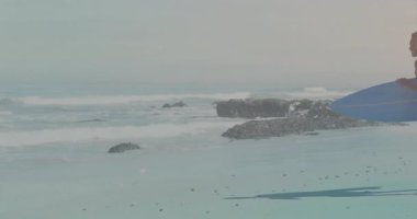 Kumlu sahil şeridinde elinde sörf tahtası olan arkadaşları kalp ikonu olan bir sağlık uygulaması gösteriyorlar. Macera, eğlence, yaşam tarzı, canlılık, hareket, açık hava, fitness