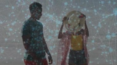 Sahilde kadınla birlikte duran bir adam dijital teknoloji ağının altında hasır şapka ayarlıyor. Teknoloji, bağlantı, arkadaşlık, eğlence, yaz, modern, açık hava