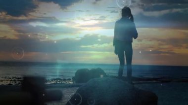 Okyanusa bakan kayaya bakan kadın gezgin teknoloji için yüzen HUD elementlerini sergiliyor. Macera, keşif, yenilik, dinginlik, doğa, gelecekçilik, manzara