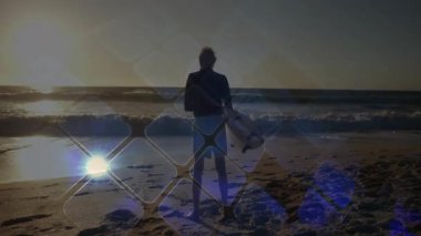 Sunset 'te sörf tahtası tutan kıdemli sörfçü elmasları gösteren teknolojiyle sahilde duruyor. Kıdemli, kıyı, sükunet, rahatlık, yansıma, minimalist, enerjik