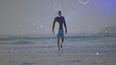 Olgun bir adam, sörf tahtası üzerinde yürüyen bir kıyı şeridi tutuyor. Yüksek çözünürlüklü grafikler, teknolojide sörf verilerini gösteriyor. Okyanus, sahil, dijital, teknoloji, macera, fitness, manzara