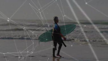 Kıdemli bayan sörfçü plaj boyunca teknolojiyle donatılmış deniz mavisi sörf tahtası taşıyor. Macera, sağlık, güç, aktif giysi, doğa, bağlantı, farkındalık.