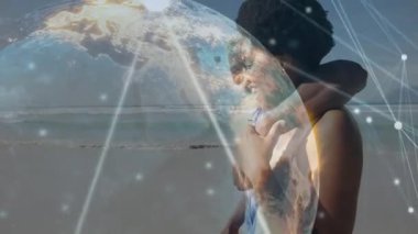 Sahilde kol kola yürüyen bir çift. Parlayan dijital küreyi kullanarak teknoloji ağı kuruyorlar. Romantizm, bağlantı, dijital, teknoloji, manzara, açık hava, uyum