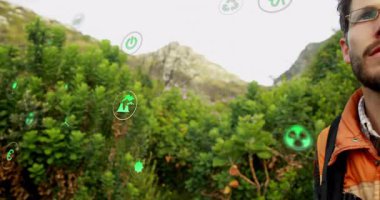 Erkek yürüyüşçü, yeşil teknoloji için yüzen yeşil AR enerji simgeleriyle etkileşime geçiyor. Macera, sürdürülebilirlik, keşif, doğa, yenilik, açık hava, çevre