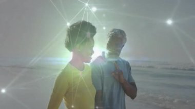 Erkek ve kadın kumlu kıyı şeridi boyunca yürüyorlar, dijital teknoloji ağını parlayan düğümlerle gösteriyorlar. Açık hava, kıyı, bağlantı, teknoloji, aile, iletişim, sağlık