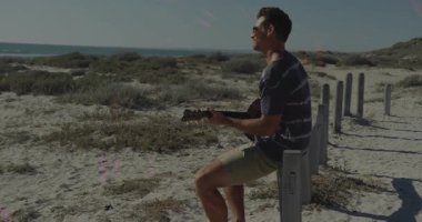 Kumlu kumullarda akustik gitar çalan bir adam, dönen pembe müzik teknolojisi ışıkları gösteriyor. Strumming, boş zaman, rahatlama, açık hava, canlı, eğlence, sükunet