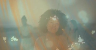 Arkadaşlar alacakaranlıkta plajda maytap tutuyorlar. Canlandırılmış kıvılcım simgeleri iş büyümesini vurguluyor. Kutlama, neşe, açık hava, alacakaranlık, yaz, parti, birliktelik