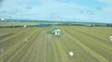 Buğday tarlasını biçen biçerdöver, yüzen telemetri simgelerini ve hareket eden tarım araçlarını gösterir. Tarım, sürdürülebilirlik, yenilik, makine, manzara, veri, tarım