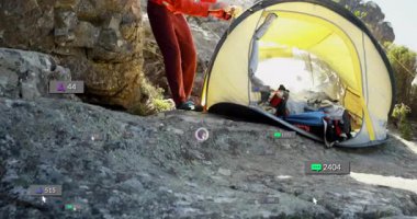 Kayanın yanında sarı çadır hattı olan bir adam yüzen sosyal medya pazarlama simgeleri sergiliyor. Macera, açık hava, engebeli, keşif, doğa, manzara, dayanıklılık.