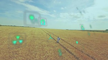 Olgun bir adam buğday tarlasında traktör izlerinin üzerinde duruyor, yüzen yenilenebilir enerji ikonlarına bakıyor. Sürdürülebilirlik, çevre, yenilik, çevre dostu, izleme, kırsal, gelecekçi