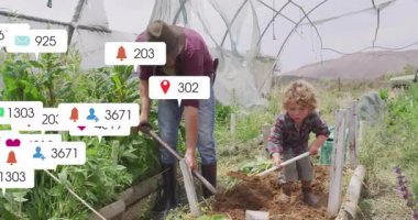 Erkek bahçıvan ve çocuk serada toprağı çeviriyor, yüzen sosyal medya pazarlama ikonları gösteriyor. Bahçe işleri, aile, yenilik, çevre dostu, takım çalışması, doğa, büyüme