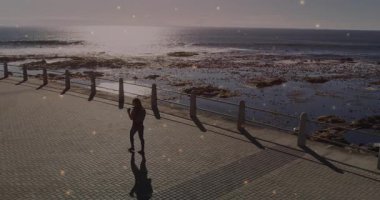 Kadın sahil yolunda yürüyor, yüzen akıllı telefon simgeleri ve pazarlama için grafik animasyonları gösteriyor. Deniz kenarı, gezinti güvertesi, güneş ışığı, boş zaman, açık hava, moda, modern