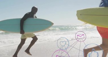 Erkek sörfçü, yüzen sosyal medya simgeleriyle kıyı şeridi boyunca yürüyor ve pazarlama teknolojisini geliştiriyor. Sahil, kıyı şeridi, dijital, teknoloji, fitness, açık hava, yaşam tarzı