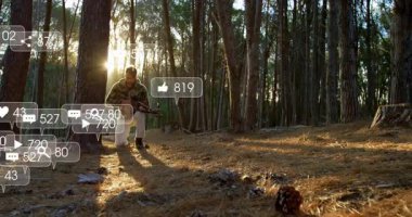 Erkek gün batımında çam ormanında diz çöküp yaylı tüfeği hedef alarak yüzen pazarlama simgelerini gösteriyor. Avcılık, vahşi doğa, doğa, macera, açık hava, hedefli, taktik