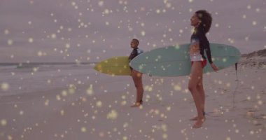 Sörf tahtası tutan dişi sörfçüler yüzen altın bokeh 'i gösteren kol plajı spor animasyonlarını kaldırıyorlar. Plaj, macera, atletik, açık hava, yaz, eğlence, canlılık