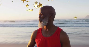 Güneş doğarken kumlu sahilde sakince duran bir adam yüzen altın yıldızlarla sağlık konseptini sergiliyor. Huzur, sağlık, farkındalık, rahatlama, ilham, sükunet, sahil kenarı.