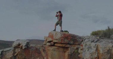 Dürbün kullanarak erkek yürüyüşçü uçurumda ufku tarıyor, animasyon teknolojisi çizelgeleri ve veri örtüsüyle. Macera, keşif, engebeli, vahşi doğa, açık hava, manzara, keşif