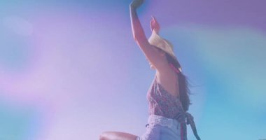 Kadın açık havada kollarını kaldırıyor hasır şapka, kot şort, hareketli pastel ışma teknolojisi gösteriyor. Botanik, moda, pastel, açık hava, canlı, kaygısız, boş zaman