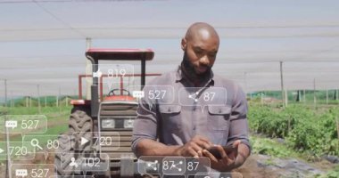 Çiftlikteki kırmızı traktörün akıllı telefonunu dinleyen orta yaşlı bir çiftçi. Ekinlerin üzerinde sosyal simgeler geziniyor. Tarım, teknoloji, kırsal, yenilik, sürdürülebilirlik, verimlilik, manzara