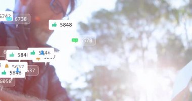 Gözlüklü bir adam, ormanda duran sırt çantası, pazarlama için yüzen sosyal simgeleri izleyen. Açık hava, teknoloji, bağlantı, doğa, iletişim, ağ, yaşam tarzı