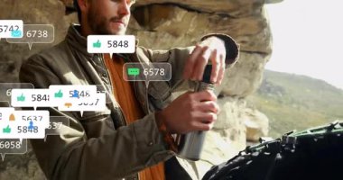 Kayalık çıkıntının altında içme suyu içen yetişkin yürüyüşçü, yüzen sosyal medya pazarlama simgeleri gösteriyor. Macera, keşif, vahşi doğa, açık hava ekipmanları, dijital kaplama, modern teknoloji, doğal manzara