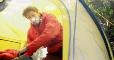 Erkek kampçı sarı çadırın içinde sırt çantasına uzanıyor, yüzen sosyal medya analiz simgeleri sergiliyor. Macera, keşif, açık hava, vahşi doğa, huzur, teknoloji.