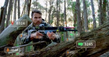 Yetişkin bir adam çam ormanında yaylı tüfekle AR teknolojisi ikonları kullanarak kütüğün arkasında yatıyor. Kamuflaj, hassasiyet, koruma, açık hava, teknoloji, gözetim, vahşi doğa.