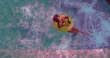 Havuzun üzerinde süzülen sarı şişme yüzüklü kadın pazarlama için neon ışıklı izler sergiliyor. Havadan, sudan, canlı, soyut, boş, dalgın, renkli.