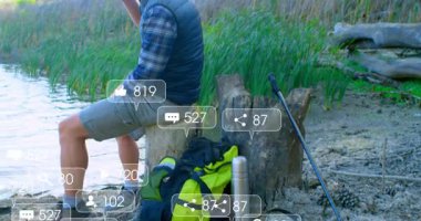 Göl kıyısında metal bardaktan yudumlayan bir adam, sırt çantasından yükselen animasyon sağlık çizelgesiyle. Doğa, macera, vahşi doğa, sükunet, açık hava, manzara, keşif