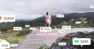 Yoga pratisyeni ahşap güvertede pembe minder üzerinde dengede duruyor, AR UI kaplamalı fitness teknolojisi kullanıyor. Zen, farkındalık, teknoloji, doğa, rahatlama, uyum, yenilik