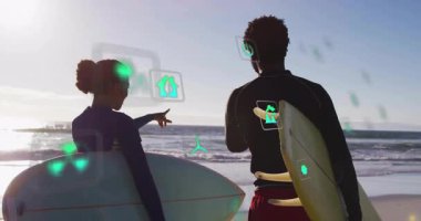 Plajda sörf tahtası tutan sörfçüler rüzgar türbini teknolojisinde yüzen yeşil enerji simgelerini gösteriyorlar. Macera, açık hava, canlılık, işbirliği, çevre, uyum, eğlence