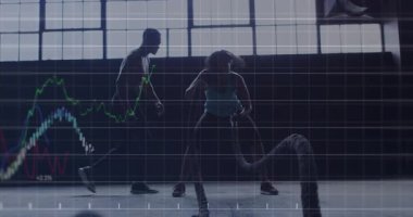 Antrenör, finans tablosu eşliğinde savaş halatı egzersizi yapan kadın stajyere rehberlik ediyor. Fitness, antrenman, güç, egzersiz, endüstriyel, motivasyon, sağlık