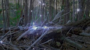 Çam ormanlarında ağaçların arkasına çömelmiş bir adam savunma simülasyonu için tüfek ve dijital ışıltılar gösteriyor. Vahşi doğa, kamuflaj, taktik, macera, doğa, dayanıklı, gizlilik.