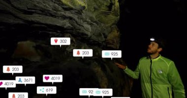 Yeşil ceketli bir kaşif mağara duvarını inceliyor, yüzen sosyal medya pazarlama ikonlarına bakıyor. Macera, keşif, teknoloji, açık hava, engebeli, dijital, keşif ekipmanları